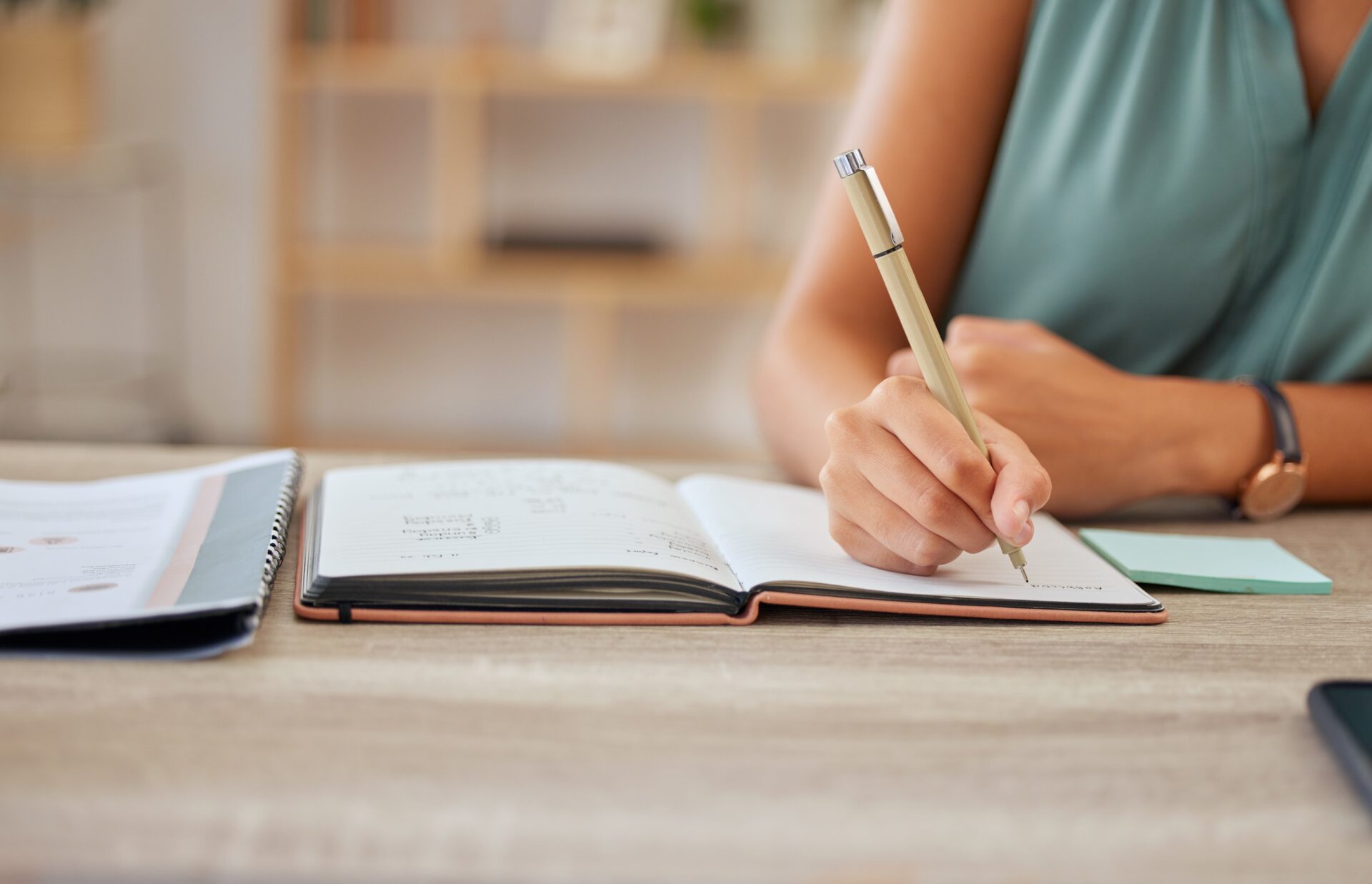 Hand, pen and writing in a notebook with a business woman sitting at a desk in her office for planning