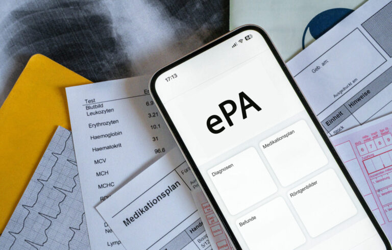Ein Smartphone auf dem gerade eine elektronische Patientenakte angezeigt wird, liegt auf medizinischen Dokumenten, horizontal