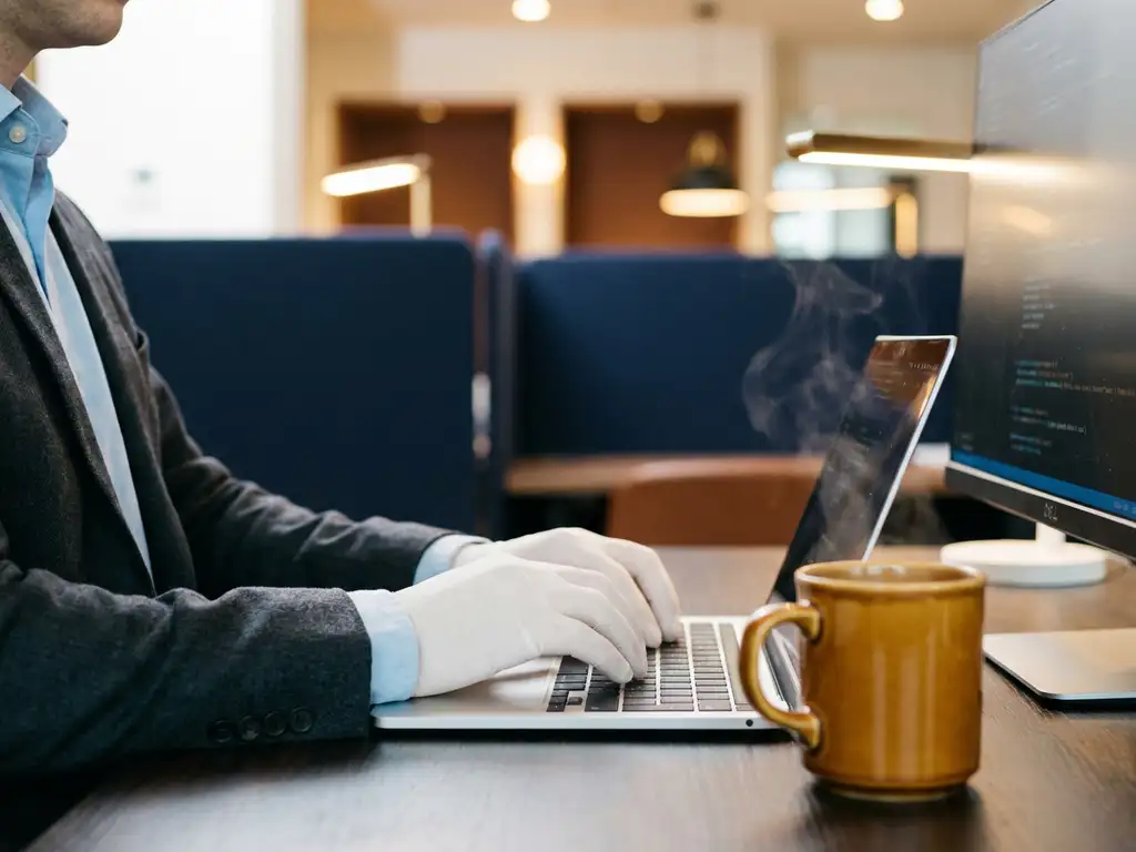 Hände tippen auf Laptop-Tastatur am modernen Schreibtisch mit glühendem Monitor und dampfendem Kaffee in Büroumgebung.